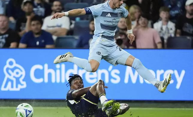 Sporting Kansas City midfielder Erik Thommy, top, leaps over Vancouver Whitecaps defender Edier Ocampo during the first half of an MLS soccer match Saturday, Sept. 20, 2025, in Kansas City, Kan. (AP Photo/Charlie Riedel)
