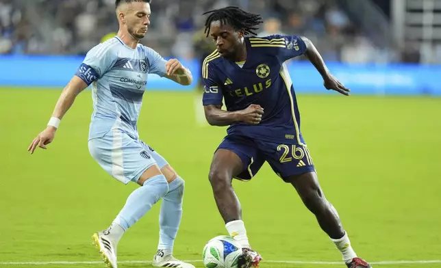 Vancouver Whitecaps midfielder Jean-Claude Ngando (26) kicks the ball past Sporting Kansas City midfielder Erik Thommy, left, during the second half of an MLS soccer match Saturday, Sept. 20, 2025, in Kansas City, Kan. (AP Photo/Charlie Riedel)