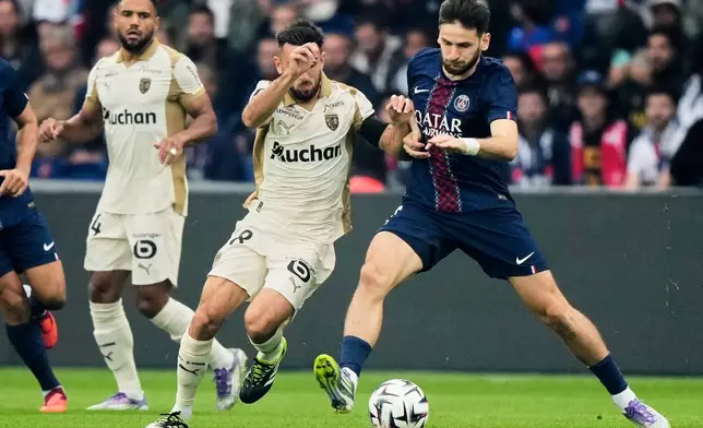 Lens' Adrien Thomasson, left, challenges for the ball with PSG's Khvicha Kvaratskhelia, right, during the French League One soccer match between Paris Saint-Germain and Lens at the Parc des Princes stadium in Paris, Sunday, Sept. 14, 2025. (AP Photo/Michel Euler)