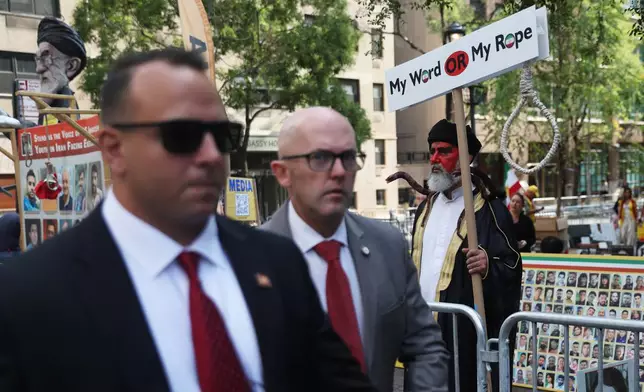 People walk past a rally against the Iranian government during the 80th session of the United Nations General Assembly, Tuesday, Sept. 23, 2025, in New York. (AP Photo/Heather Khalifa)