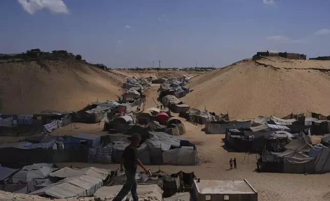 Displaced Palestinians walks through a tent camp in Muwasi, an area that Israel has designated as a safe zone, in Khan Younis southern Gaza Strip, Sunday, Sept. 21, 2025. (AP Photo/Jehad Alshrafi)