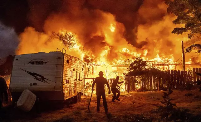 Residents work to stop flames from a burning home from spreading to a neighboring house as the 6-5 Fire burns through the Chinese Camp community of Tuolumne County, Calif., on Tuesday, Sept. 2, 2025. (AP Photo/Noah Berger)