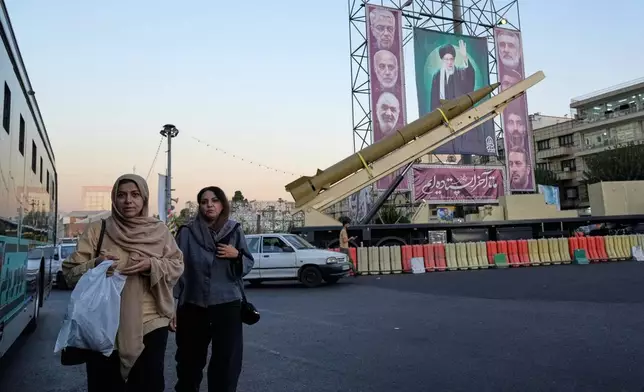 People walk past a domestically-built missile "Khaibar-buster," and banners showing portraits of the Iranian Supreme Leader Ayatollah Ali Khamenei, center, and the late armed forces commanders, who were killed in Israeli strike in June, displayed in a military exhibition commemorating the anniversary of the start of the 1980-88 Iraq-Iran war, and 12-day war with Israel in June, at Baharestan Square in Tehran, Thursday, Sept. 25, 2025. (AP Photo/Vahid Salemi)