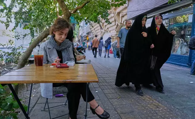 A woman sits in the al fresco dining area of a cafe at the Enqelab-e-Eslami (Islamic Revolution) street, in Tehran, Iran, Saturday, Sept. 27, 2025. (AP Photo/Vahid Salemi)