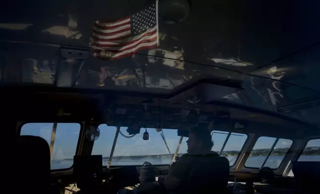 An American flag is reflected in the windows of the bridge as mate Peter Emery pilots the Gaspee, a crew transport vessel, along the Sakonnet River near Portsmouth, R.I., during the eight-hour trip to the Liftboat Robert platform and Expedition 501 in the North Atlantic, Saturday, July 19, 2025. (AP Photo/Carolyn Kaster)