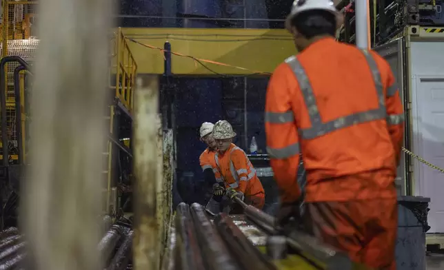 Expedition 501 drilling team members, from left, Nick Boehne, Chris Redding and Lalo Aguilar work to remove a core sample from an inner tube during a wireline core drilling operation aboard the Liftboat Robert platform, in the North Atlantic, Sunday, July 20, 2025. (AP Photo/Carolyn Kaster)