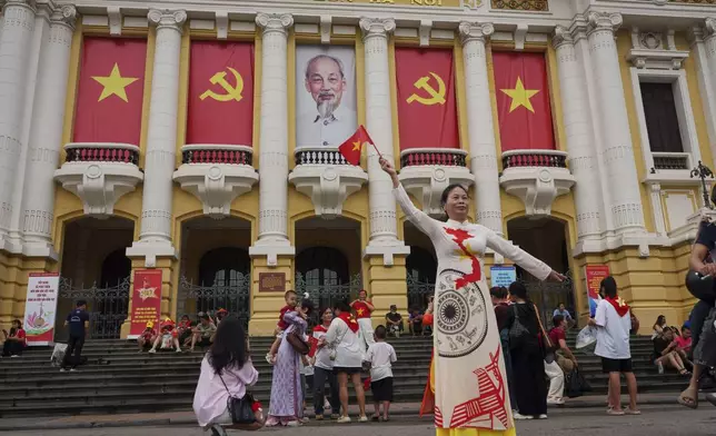 A Vietnamese woman stands for a photograph in front of the Opera House, its balconies decorated with Vietnamese and communist flags in the old quarter of Hanoi, Vietnam, Monday, Sept. 1, 2025. (AP Photo/Vincent Thian)