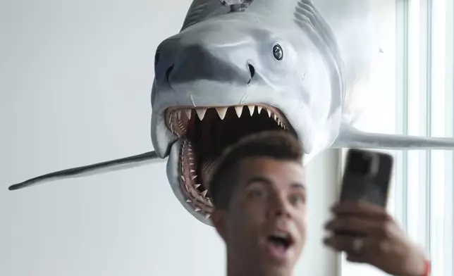A visitor to the "Jaws: The Exhibition" press preview shoots a selfie underneath the sole surviving full-scale model of "Bruce," the shark from the 1975 film, on Wednesday, Sept. 10, 2025, at the Academy Museum of Motion Pictures in Los Angeles. (AP Photo/Chris Pizzello)