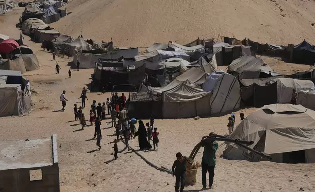 Displaced Palestinians walks through a tent camp in Muwasi, an area that Israel has designated as a safe zone, in Khan Younis southern Gaza Strip, Sunday, Sept. 21, 2025. (AP Photo/Jehad Alshrafi)