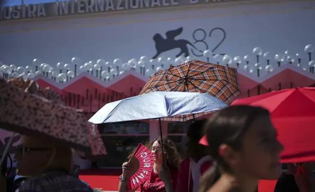 Festival goers shelter from the sun as they wait for arrivals on the red carpet for the film 'The Wizard of the Kremlin' during the 82nd edition of the Venice Film Festival in Venice, Italy, on Sunday, Aug. 31, 2025. (Photo by Alessandra Tarantino/Invision/AP)