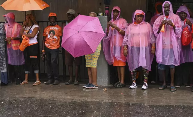 Supporters of the People's National Party wait in line in the rain outside a polling station to vote during general elections in Kingston, Jamaica, Wednesday, Sept. 3, 2025. (AP Photo/Collin Reid)