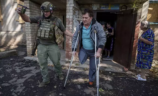 A police officer helps Mykhailo Maistruk, 67, during evacuation from Kostiantynivka, Ukraine, Tuesday, Sept. 2, 2025. (AP Photo/Evgeniy Maloletka)