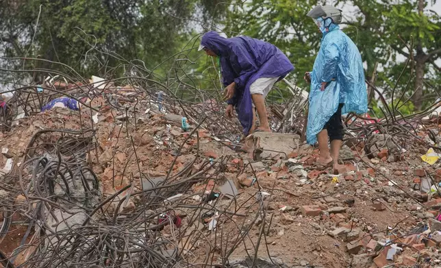 Family members stand on debris at the site of a 10-story condo that collapsed during the March 28 earthquake, in Mandalay, Myanmar, Aug. 27, 2025. (AP Photo/Aung Shine Oo)