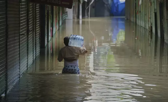 A person wades through flooded water carrying drinking water battles for the residents stuck in their house after the river Yamuna, swollen by incessant rain in the higher regions, overran its banks, in New Delhi, India, Friday, Sept. 5, 2025. (AP Photo/Manish Swarup)