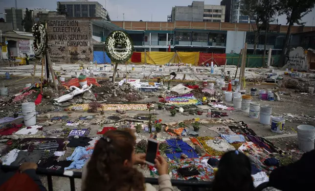 FILE - Clothing, cloth, and flowers are arranged in a memorial that includes the messages in Spanish: "Our lives matter" and "Our bodies are not trash," at the site of a textile factory that collapsed in an earthquake in Mexico City, Sept. 25, 2017. (AP Photo/Rebecca Blackwell, File)