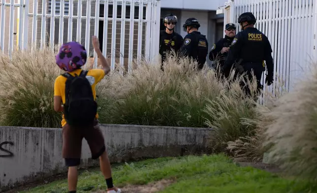 A protester waves to Department of Homeland Security officials as they walk to the gates of the U.S. Immigration and Customs Enforcement facility after inspecting an area outside on Sunday, Sept. 28, 2025, in Portland, Ore. (AP Photo/Jenny Kane)