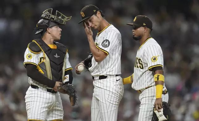 San Diego Padres starting pitcher Yu Darvish wipes his face as meets on the mound with catcher Freddy Fermin, left, and first baseman Luis Arraez during the fifth inning of a baseball game against the Baltimore Orioles Tuesday, Sept. 2, 2025, in San Diego. (AP Photo/Gregory Bull)