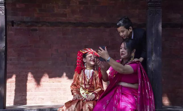 A Newar woman takes a selfie with her young daughter, dressed to represent divine female energy, and her son as they wait for Kumari Puja, a ritual during which the young girl would be worshipped, at Hanuman Dhoka, Basantapur Durbar Square, Kathmandu, Nepal, Friday, Sept. 5, 2025. (AP Photo/Niranjan Shrestha)