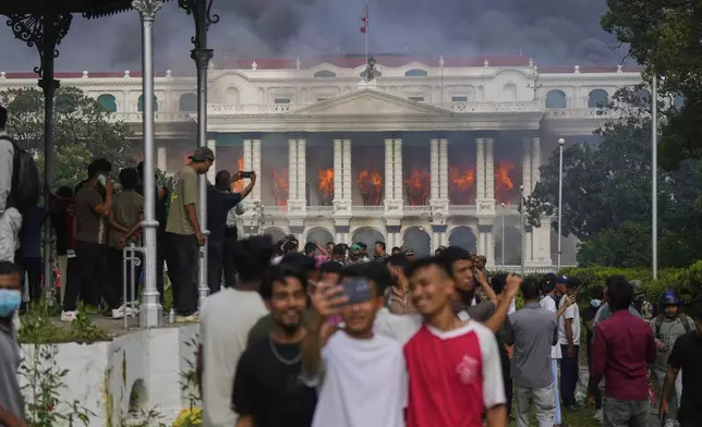 Protesters take selfies and celebrate at the Singha Durbar, the seat of Nepal's government's various ministries and offices, after it was set on fire during a protest against social media ban and corruption in Kathmandu, Nepal, Tuesday, Sept. 9, 2025. (AP Photo/Niranjan Shrestha)