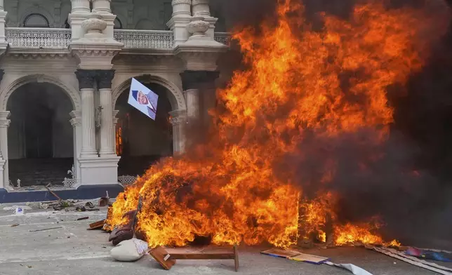 A protester throws a photograph of Nepal Prime Minister Khadga Prasad Oli in the fire at the Singha Durbar, the seat of Nepal's government's various ministries and offices during a protest against social media ban and corruption in Kathmandu, Nepal, Tuesday, Sept. 9, 2025. (AP Photo/Niranjan Shrestha)
