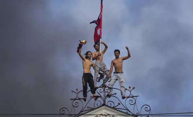 Protesters celebrate standing at the top of the Singha Durbar, the seat of Nepal's government's various ministries and offices, after it was set on fire during a protest against social media ban and corruption in Kathmandu, Nepal, Tuesday, Sept. 9, 2025. (AP Photo/Niranjan Shrestha)