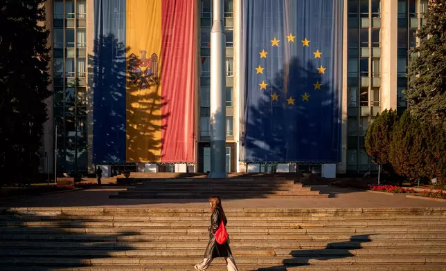 A woman walks in front of the government building, decorated with European Union and Moldovan flags, in Chisinau, Moldova, Friday, Sept. 26, 2025, ahead of parliamentary elections taking place on Sept. 28. (AP Photo/Vadim Ghirda)