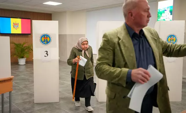 A woman exiting a voting booth waits in line to cast her vote during a parliamentary election, in Chisinau, Moldova, Sunday, Sept. 28, 2025. (AP Photo/Vadim Ghirda)
