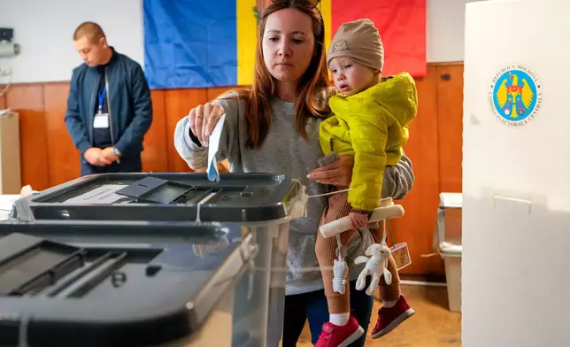 A woman holds a child as she casts her vote during a parliamentary election, in Chisinau, Moldova, Sunday, Sept. 28, 2025. (AP Photo/Vadim Ghirda)