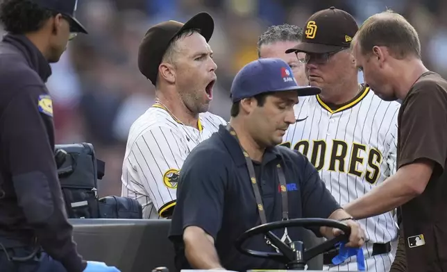San Diego Padres relief pitcher Jason Adam, second from left, reacts alongside manager Mike Shildt as he leaves in a cart after falling with an injury during the seventh inning of a baseball game against the Baltimore Orioles Monday, Sept. 1, 2025, in San Diego. (AP Photo/Gregory Bull)