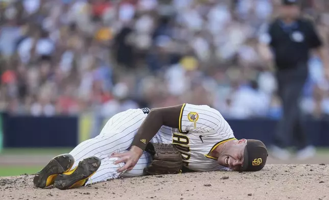 San Diego Padres relief pitcher Jason Adam holds his leg after falling with an injury during the seventh inning of a baseball game against the Baltimore Orioles Monday, Sept. 1, 2025, in San Diego. (AP Photo/Gregory Bull)