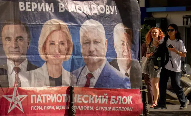 Women walk next to a campaign tent of the Patriotic Electoral Bloc with the slogan "We believe in Moldova" in Chisinau, Moldova, Tuesday, Sept. 23, 2025, ahead of parliamentary elections taking place on Sept. 28. (AP Photo/Vadim Ghirda)