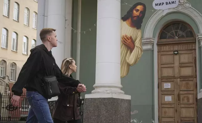 A couple walk past an image of Jesus Christ and the words 'Peace be with you!' inscribed on the column of the Lutheran Annenkirche Church in St. Petersburg, Russia, Wednesday, Sept. 17, 2025. (AP Photo/Dmitri Lovetsky)