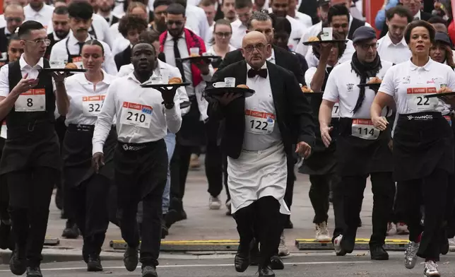 Servers carry trays with a cup of coffee, a croissant and a glass of water as they take part in a servers' race through the streets of Paris, Sunday, Sept. 21, 2025. (AP Photo/Christophe Ena)