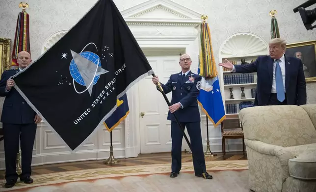 FILE - Gen. John "Jay" Raymond, Commander U.S. Space Command, left, and Chief Master Sgt. Roger Towberman, right, hold the flag as President Donald Trump gestures, during the presentation of the Space Force Flag in the Oval Office of the White House, May 15, 2020, in Washington. Secretary of the Air Force Barbara Barrett stands far left. (AP Photo/Alex Brandon, File)