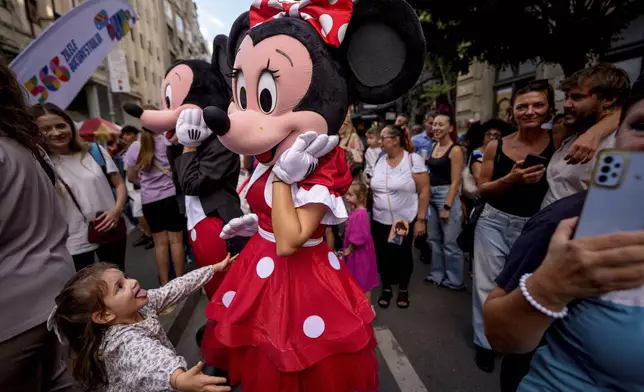 A child tries to hug an entertainer wearing a Minnie Mouse costume during a parade marking the day when the Romanian capital was first mentioned in historical records, 566 years ago, in Bucharest, Romania, Saturday, Sept. 20, 2025. (AP Photo/Andreea Alexandru)