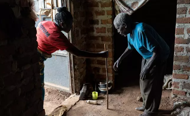 Grace Nabanoba, a field worker with Reach One Touch One Ministries, left, holds out a cane for Samuel Kakungulu, 79, during a wellness check at his home in Nkulagirire, Uganda, Friday, Nov. 15, 2024. (AP Photo/David Goldman)
