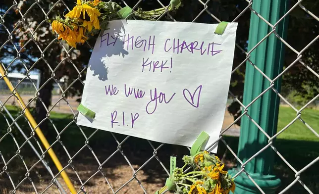 A sign reading “Fly High Charlie Kirk! We love you. R.I.P.” is seen hanging on a fence with flowers across the street from the Utah Valley University campus, in Orem, Utah, Thursday, Sept. 11, 2025. (AP Photo/Hannah Schoenbaum)