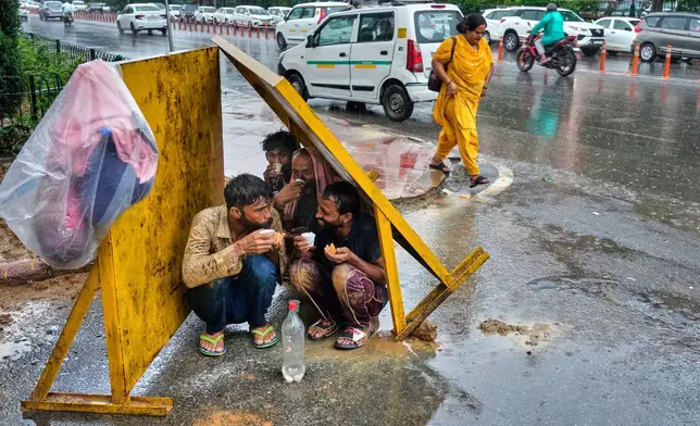 Laborers drink tea, sitting under tin shade panels to shelter themselves from the rain during roadwork, in New Delhi, India, Monday, Sept. 1, 2025. (AP Photo/Manish Swarup)