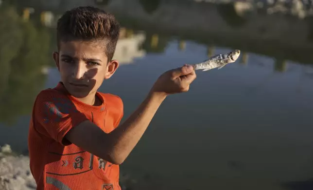 A Syrian boy holds a dead fish in the dried up Orontes River in Jisr al-Shughur, west of Idlib, Syria, on Aug. 13, 2025. (AP Photo/Omar Albam)
