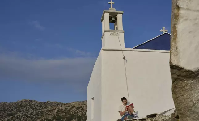 Giannis Kafantaris, 26, reads a book outside Panagia Theoskespasti, the chapel his family co-owns near the village of Falatados, on the Aegean island of Tinos, Greece, Friday, Sept. 5, 2025. (AP Photo/Petros Giannakouris)
