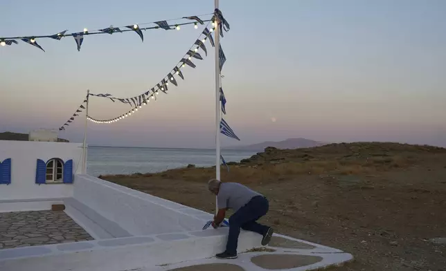 Zerar Delatolas fastens Greek flags to a pole outside the family-owned Agios Sostis chapel during its annual panigiri, on the island of Tinos, Greece, Saturday, Sept. 6, 2025. (AP Photo/Petros Giannakouris)