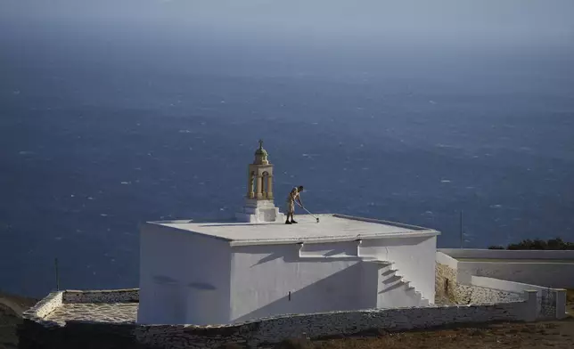 Naim Domi, 50, an Albanian worker who has lived in Greece for 17 years, paints the rooftop of the Panagia Faneromeni family-owned chapel overlooking the Aegean Sea near the village of Pyrgos, on the island of Tinos, Greece, Sunday, Sept. 7, 2025. (AP Photo/Petros Giannakouris)