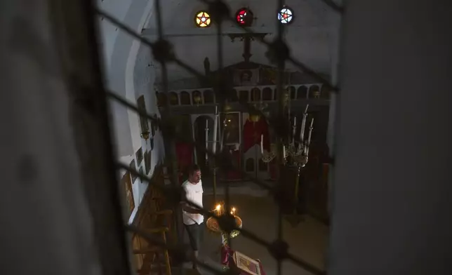 Konstantinos Vasilopoulos lights a candle at the Panagia Faneromeni family-owned chapel near the village of Triantaros, on the island of Tinos, Greece, Saturday, Sept. 6, 2025. (AP Photo/Petros Giannakouris)