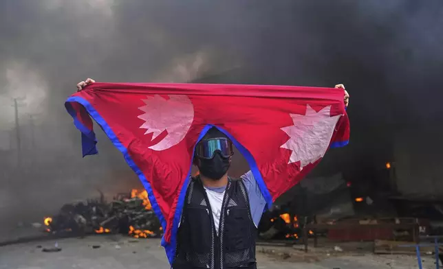 A protester shouts slogans carrying national flag after burning down a police station during protests against social media ban and corruption in Kathmandu, Nepal, Tuesday, Sept. 9, 2025. (AP Photo/Niranjan Shrestha)