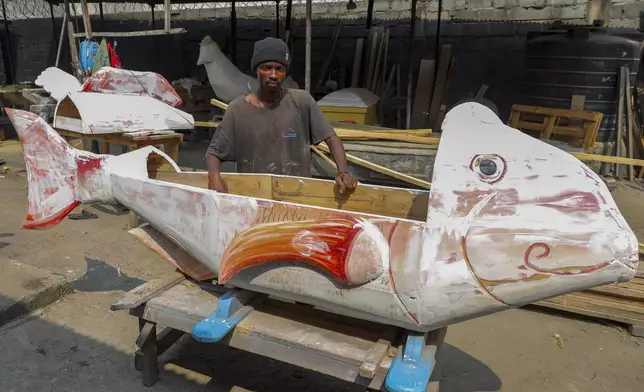 Nicholas Ablorh Annan, poses by a fish-shaped fantasy coffin in production, at his father's workshop in Teshie, Accra, Ghana, Tuesday, July 29, 2025. (AP Photo/Misper Apawu)