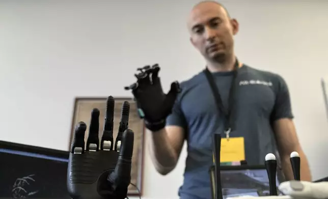 Ryan Saavedra CEO of Cortical Labs operates a bionic hand at the first International Humanoid Olympiad at the Olympic Academy, in ancient Olympia, Greece, Monday, Sept. 1, 2025. (AP Photo/Thanassis Stavrakis)