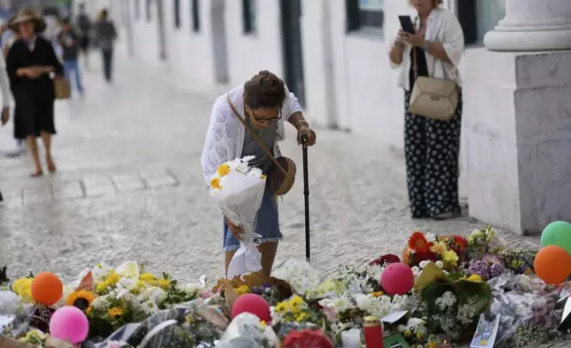 An elderly woman places a bouquet of flowers at a tribute to those that perished in the Gloria funicular, a tourist streetcar that derailed and crashed, in Lisbon, Saturday, Sept. 6, 2025. (AP Photo/Armando Franca)