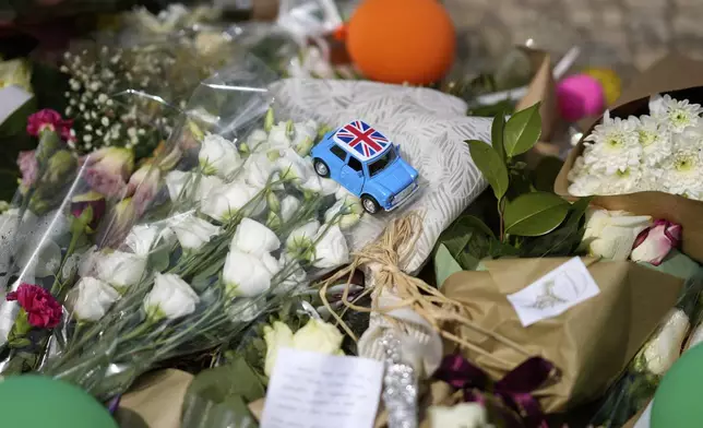 A toy with the United Kingdom flag is placed among the flowers of a tribute to those that perished in the Gloria funicular, a tourist streetcar that derailed and crashed, in Lisbon, Saturday, Sept. 6, 2025. (AP Photo/Armando Franca)