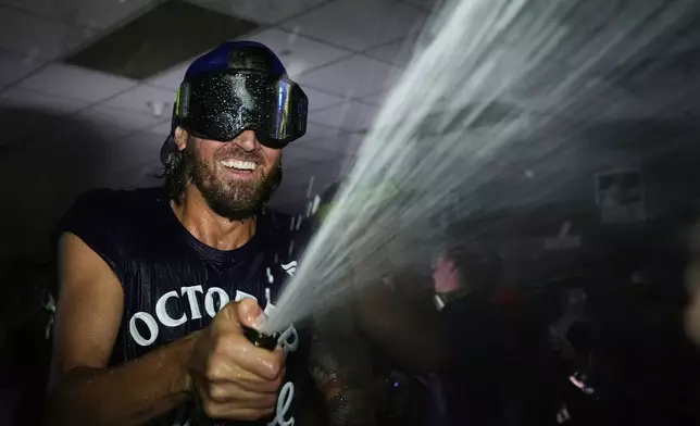 Toronto Blue Jays' Kevin Gausman celebrates with teammates in the clubhouse after their baseball game against the Kansas City Royals, Sunday, Sept. 21, 2025, in Kansas City, Mo. (AP Photo/Charlie Riedel)