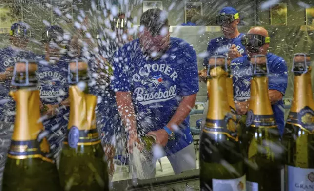 Toronto Blue Jays manager John Schneider, center, celebrates with players in the clubhouse after their a baseball game against the Kansas City Royals, Sunday, Sept. 21, 2025, in Kansas City, Mo. (AP Photo/Charlie Riedel)